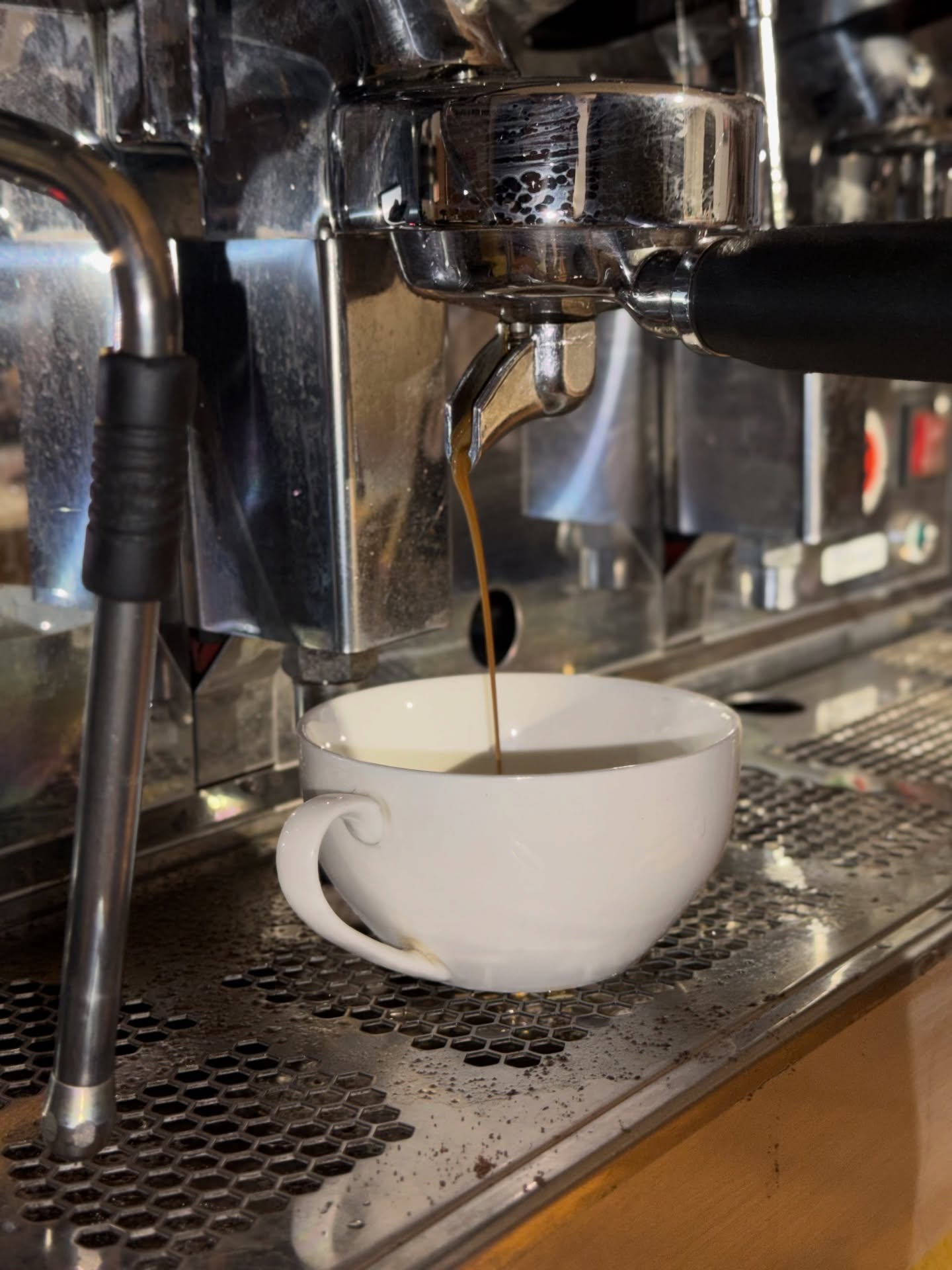 9-bar espresso extraction into ceramic cup on commercial machine at Caffinity